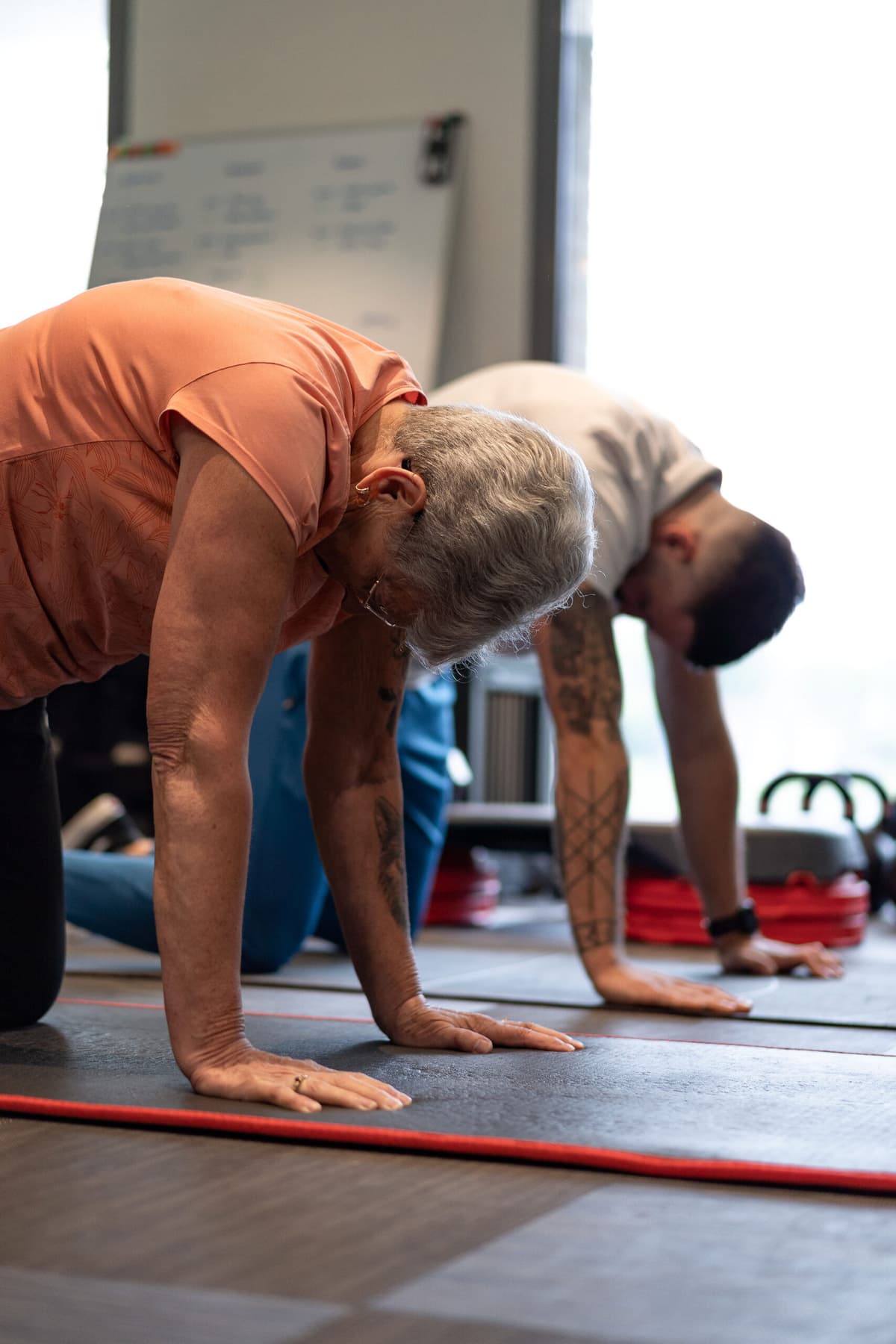 Une cliente senior réalise un exercice au sol accompagnée de son coach